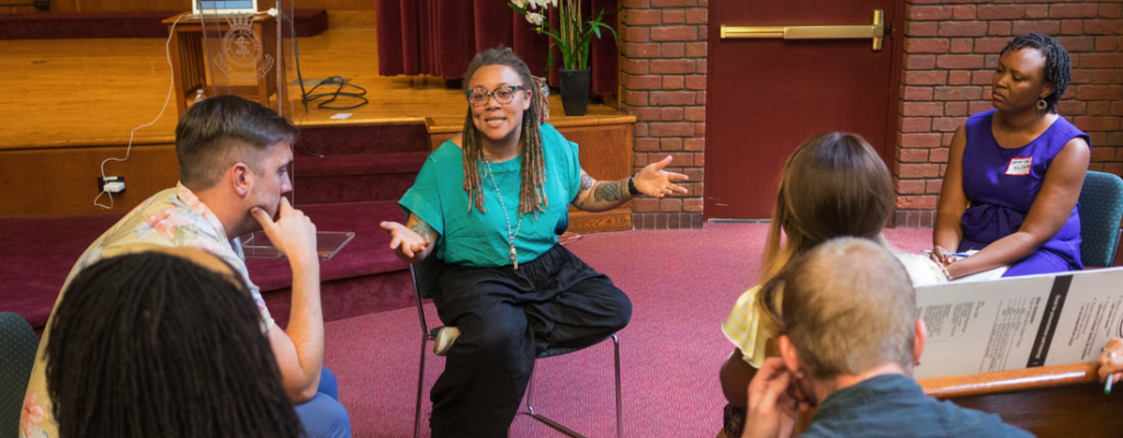 Sara Green, a young Black woman, animatedly speaks in a small group of people