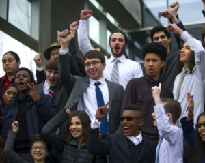 A group of children and youth of many races jubilantly raise their fists in the air