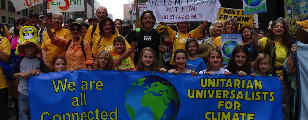 Many people of all ages hold banners and signs, one of which says "we are all connected - Unitarian Universalists for climate action"