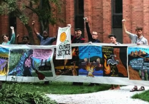 Seven young adults hold up a climate justice banner and raise fists in the air