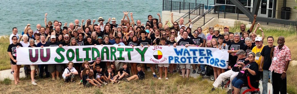 Attendees of UUA Southern Region summer camp, The Point, pose with a banner reading "UU Solidiarty with Indigenous Water Protectors", July 2018